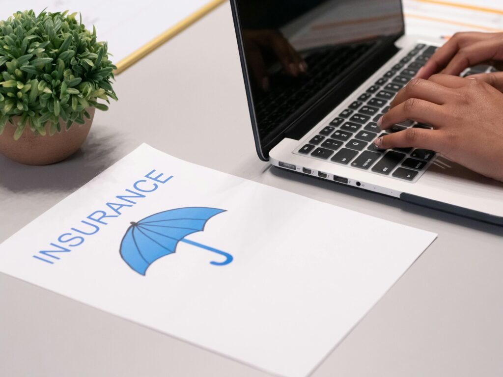 Close-up of hands typing on laptop with an insurance document visible on the desk. Fully insured including cyber protection. Affiliated with Society of Virtual Assistants