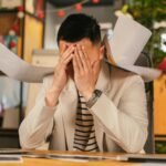 Stressed businessman overwhelmed by paperwork in office, demonstrating the need for a virtual assistant